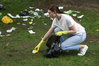 Photo of Young woman with plastic bag collecting garbage on green grass outdoors