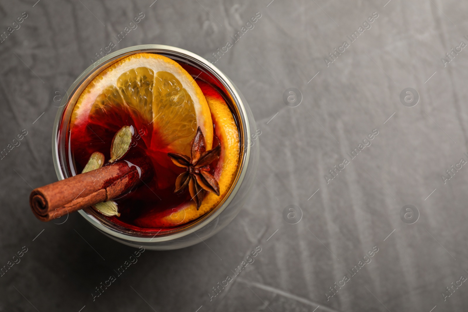 Photo of Glass with mulled wine on grey table, top view. Space for text