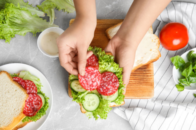 Photo of Woman making tasty sandwich at light grey marble table, top view