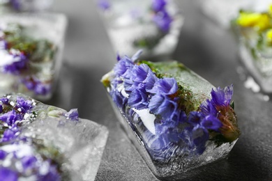 Ice cubes with flowers on grey stone table, closeup