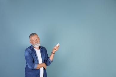 Photo of Senior man with air conditioner remote control on color background