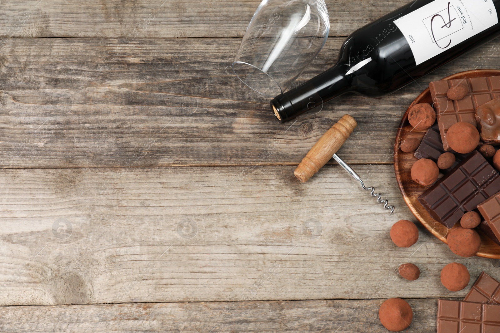 Photo of Bottle of red wine, glass, chocolate sweets and corkscrew on wooden table, flat lay. Space for text