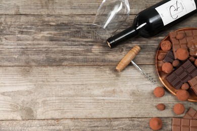 Bottle of red wine, glass, chocolate sweets and corkscrew on wooden table, flat lay. Space for text