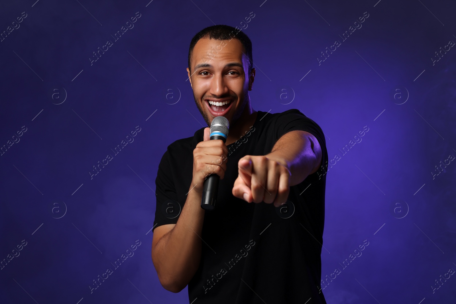 Photo of Handsome man with microphone singing on blue background