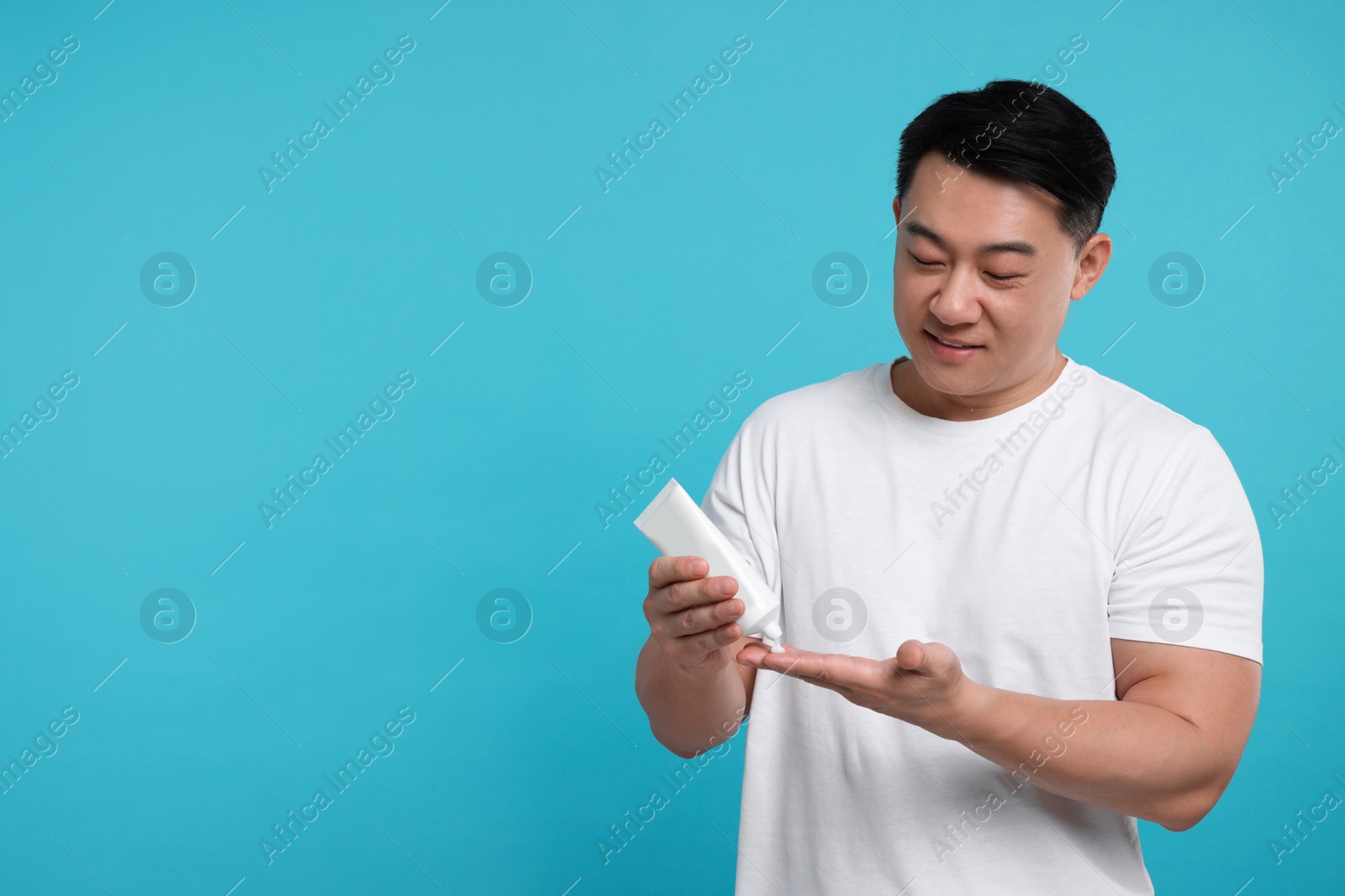 Photo of Handsome man applying body cream onto his hand on light blue background. Space for text