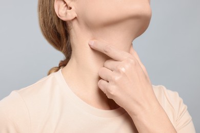 Photo of Woman suffering from sore throat on light grey background, closeup