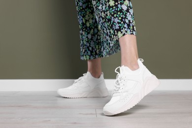 Photo of Woman wearing pair of new stylish sneakers near dark olive wall, closeup