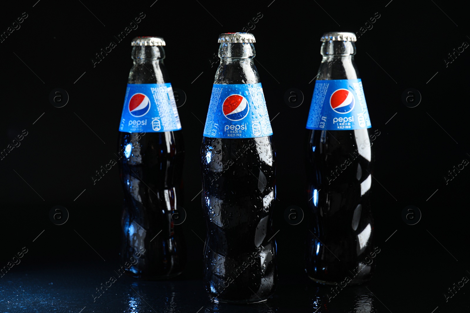 Photo of MYKOLAIV, UKRAINE - FEBRUARY 08, 2021: Glass bottles of Pepsi with water drops on black background