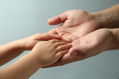 Photo of Father and child holding hands on light blue background, closeup