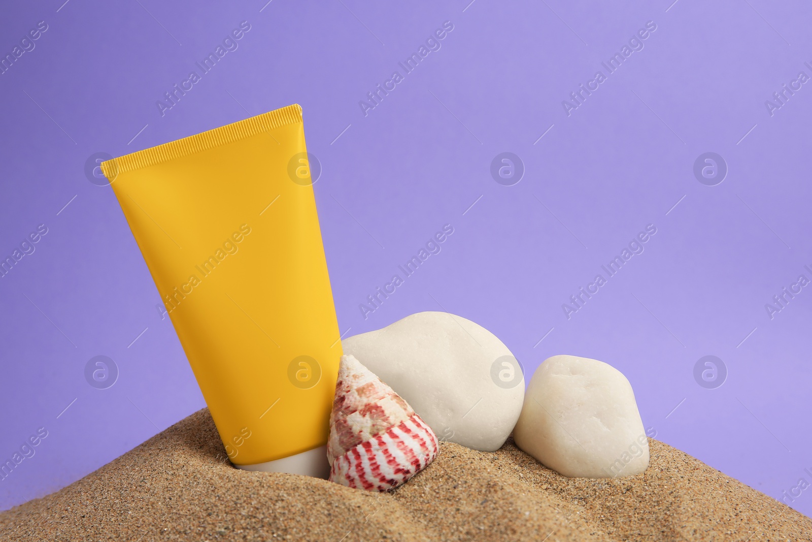 Photo of Sand with sunscreen, stones and seashell against lilac background, space for text. Sun protection care