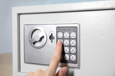 Photo of Woman dialing combination on keypad of steel safe, closeup