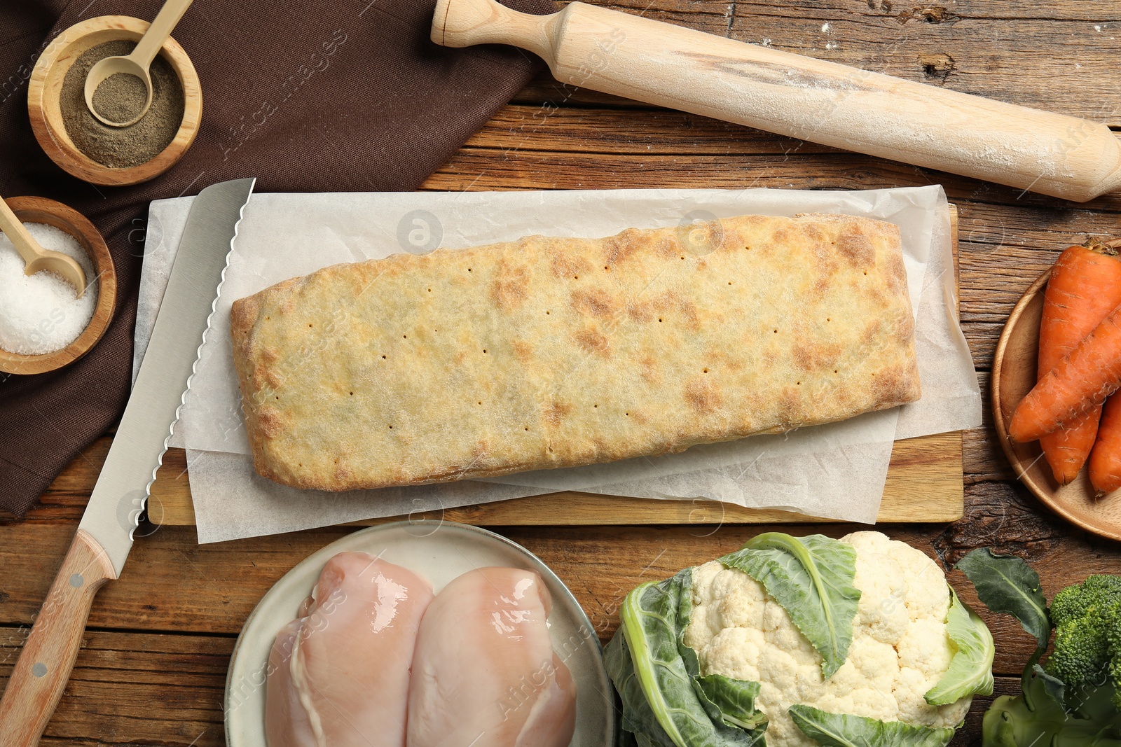 Photo of Delicious strudel with chicken and vegetables on wooden table, flat lay