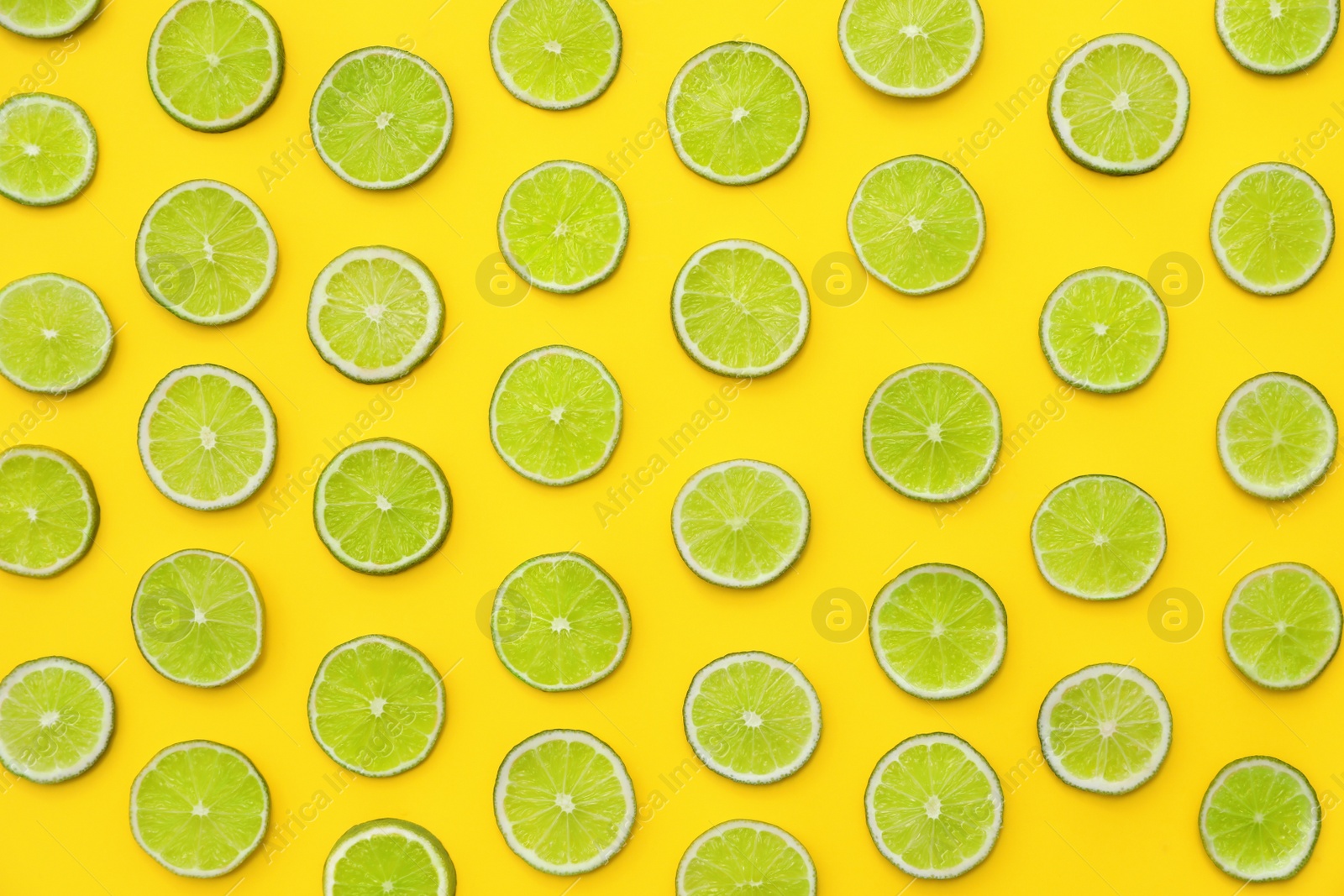 Photo of Slices of fresh juicy limes on yellow background, flat lay