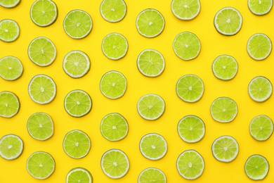 Photo of Slices of fresh juicy limes on yellow background, flat lay