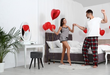 Young couple dancing in bedroom decorated with air balloons. Celebration of Saint Valentine's Day