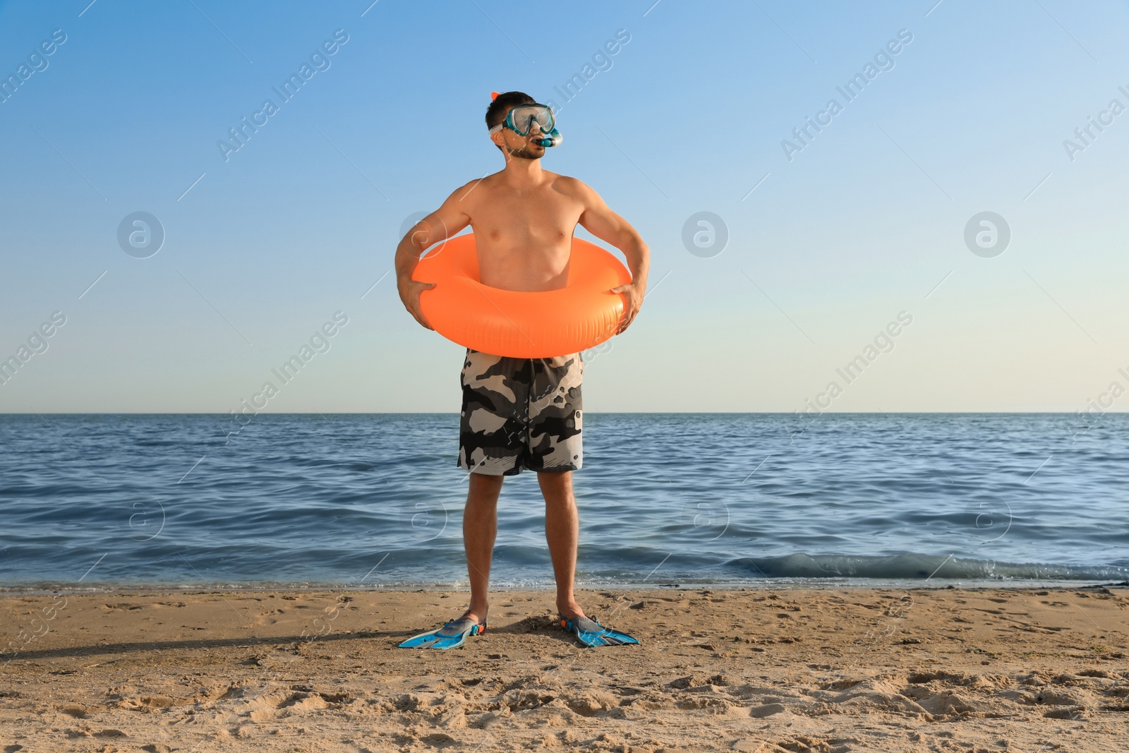 Photo of Man with flippers, inflatable ring and goggles on sea beach