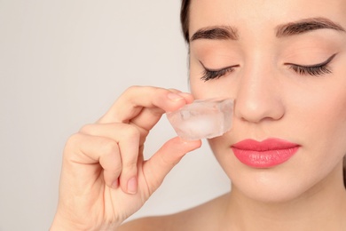 Photo of Young woman with ice cube on light background. Skin care