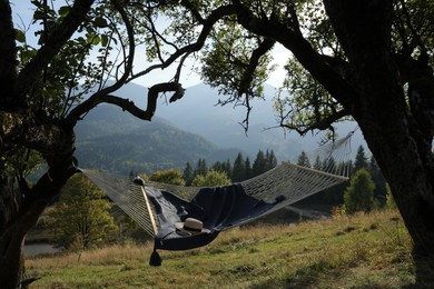 Comfortable net hammock with hat, book and blanket in mountains on sunny day