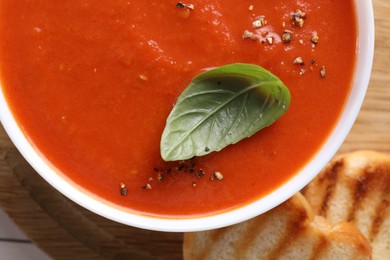 Delicious tomato soup with basil, spices and bread on table, top view