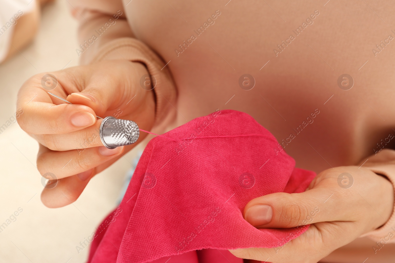 Photo of Woman sewing on red fabric with thimble and needle, closeup