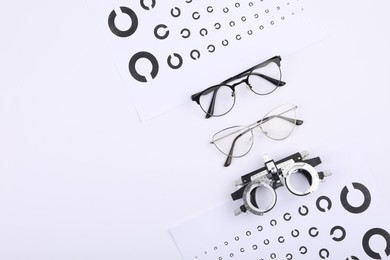 Photo of Vision test charts, glasses and trial frame on white background, flat lay. Space for text