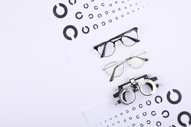 Vision test charts, glasses and trial frame on white background, flat lay. Space for text