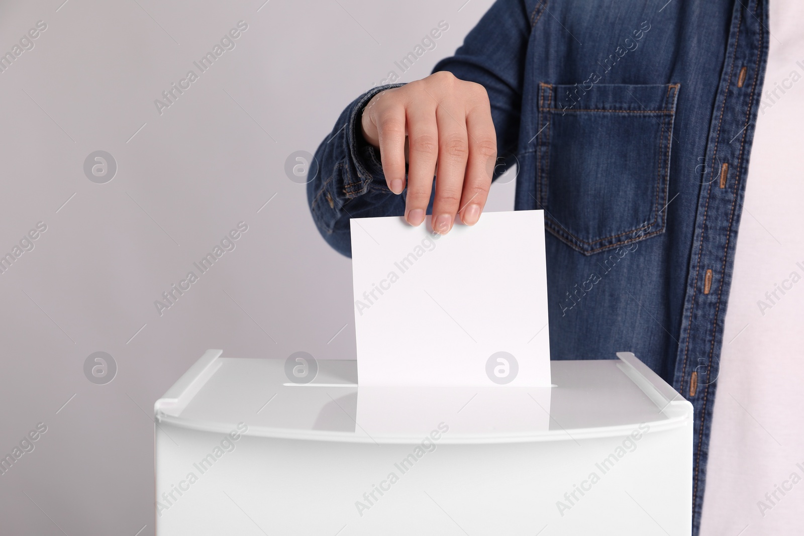 Photo of Woman putting her vote into ballot box on light grey background, closeup