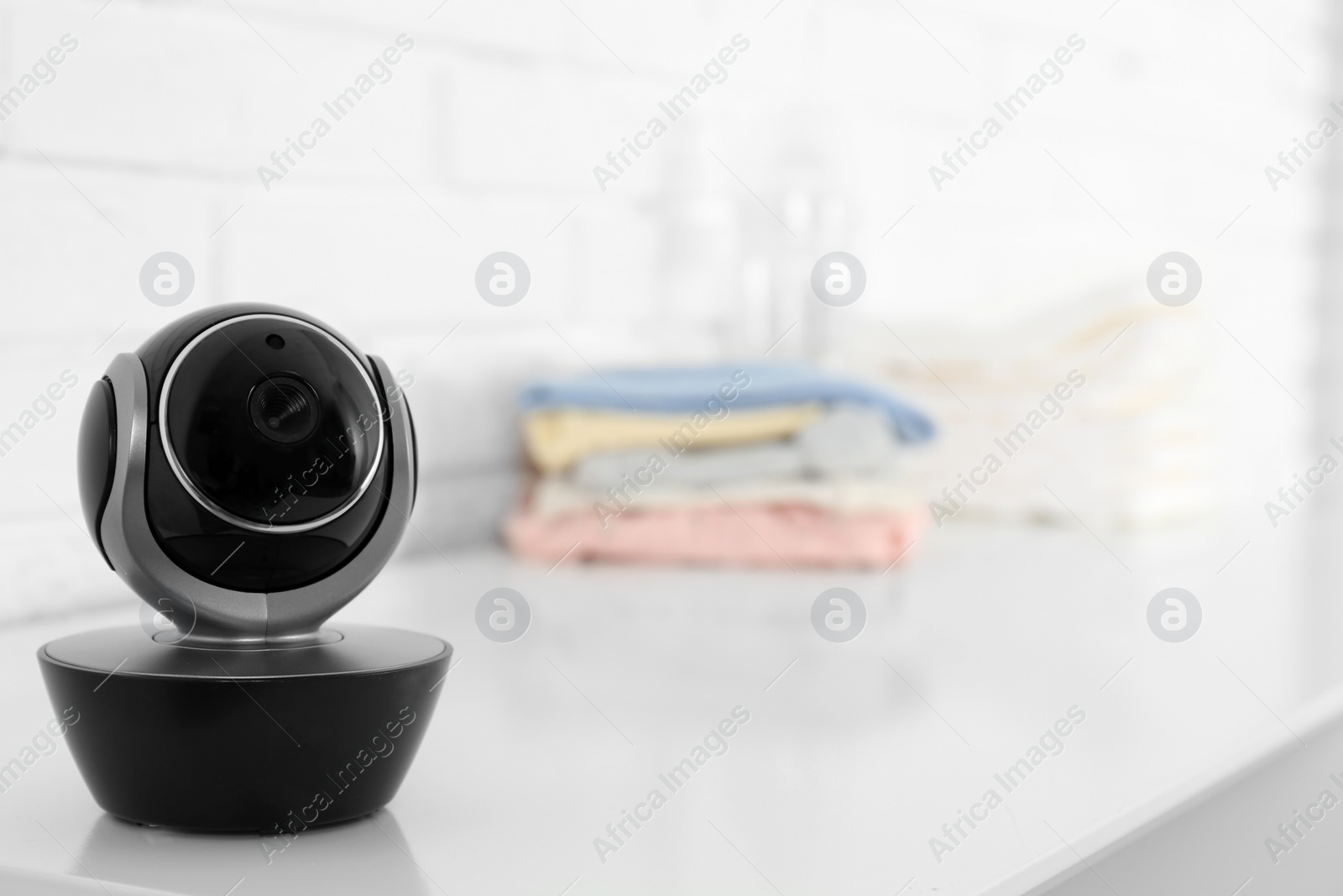 Photo of Baby camera on table near white brick wall, space for text. Video nanny