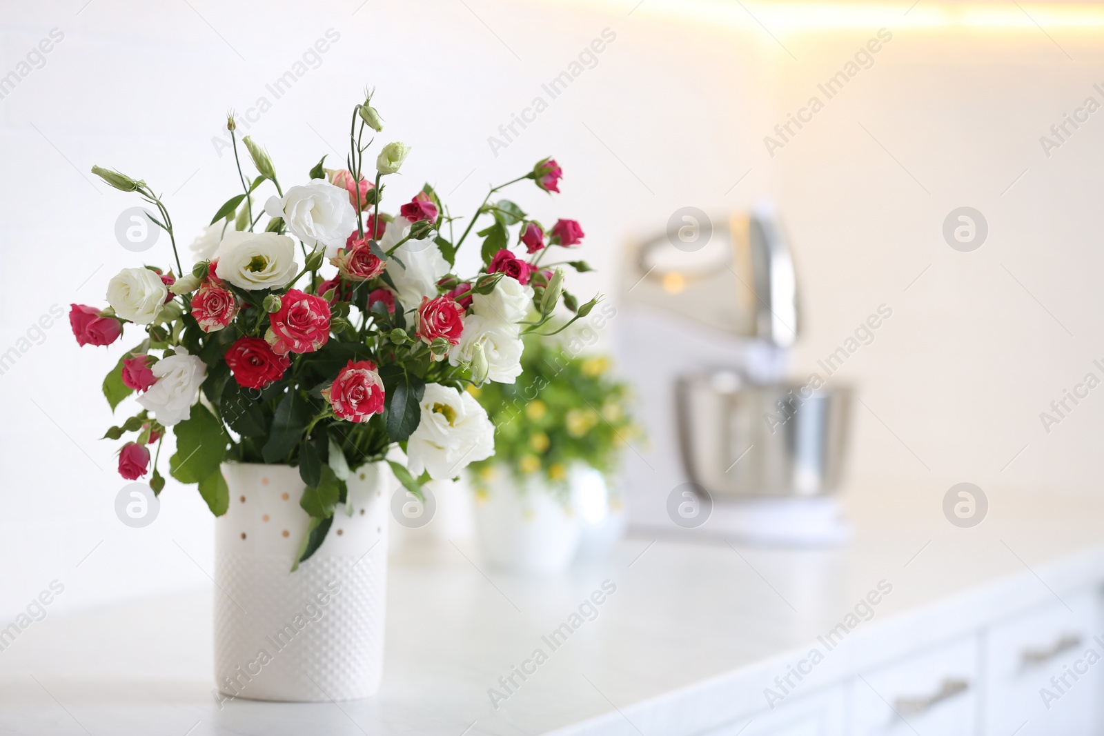 Photo of Vase with beautiful flowers on white countertop in kitchen, space for text