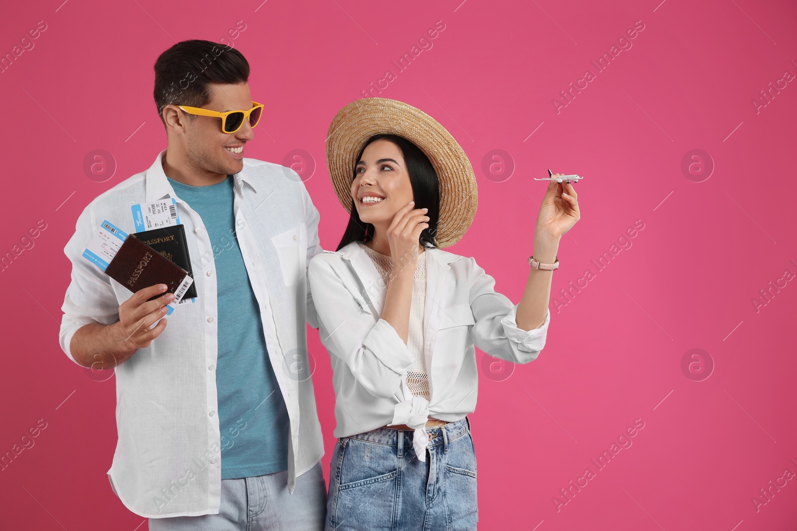 Photo of Couple of tourists with tickets, passports and toy plane on pink background