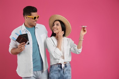 Couple of tourists with tickets, passports and toy plane on pink background