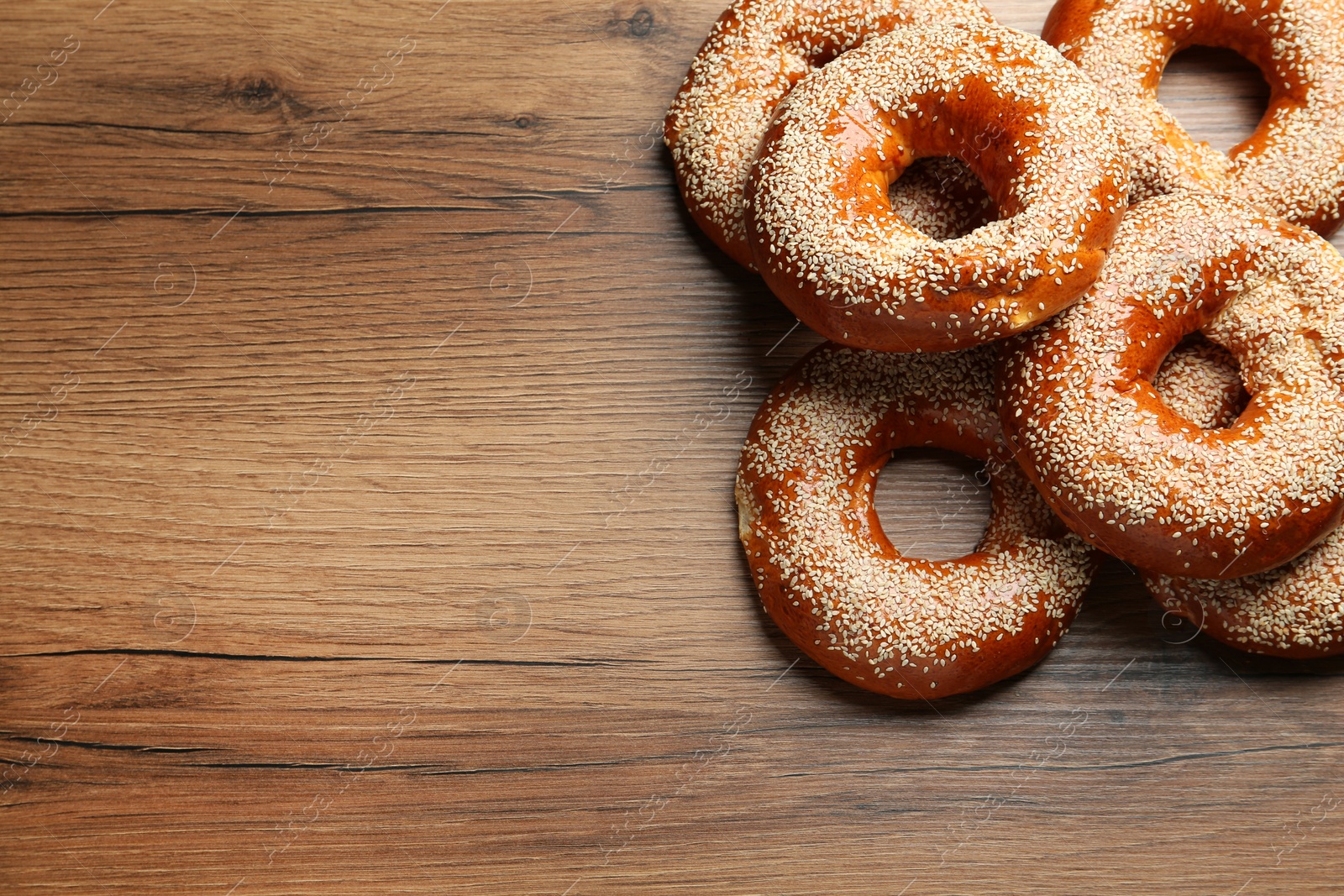 Photo of Delicious fresh bagels with sesame seeds on wooden table, flat lay. Space for text