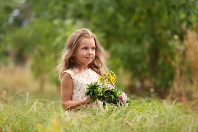 Photo of Cute little girl holding wreath made of beautiful flowers in field