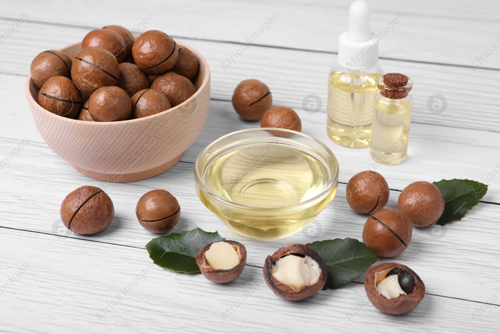 Photo of Delicious organic Macadamia nuts and cosmetic oil on white wooden table