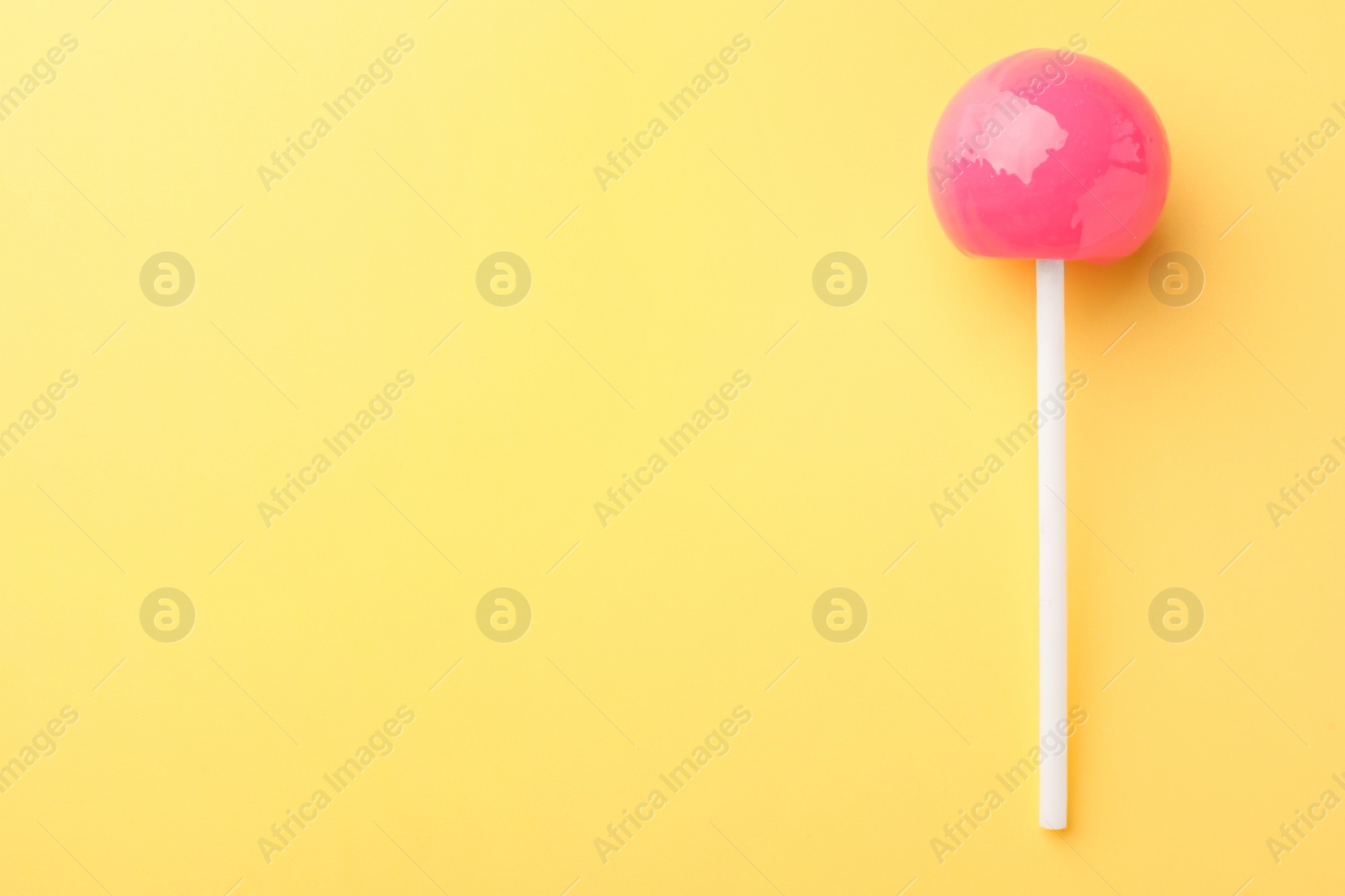 Photo of One tasty lollipop on yellow background, top view. Space for text