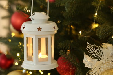 Photo of Christmas lantern with burning candle on fir tree as background, closeup