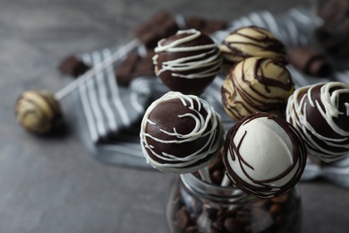 Yummy cake pops coated with chocolate in glass jar on table, closeup. Space for text