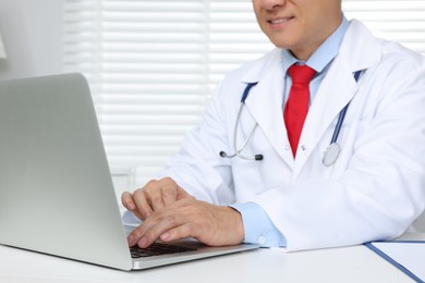 Photo of Doctor working with laptop at white desk in clinic, closeup. Online medicine