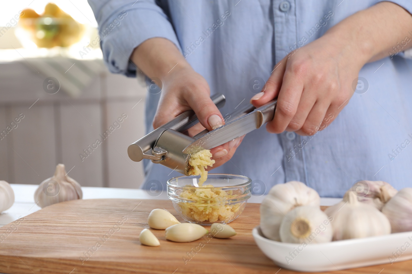 Photo of Woman squeezing garlic with press at wooden table indoors, closeup