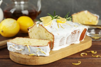 Tasty lemon cake with glaze and citrus fruits on wooden table, closeup