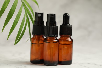 Photo of Bottles of organic cosmetic products and green leaves on light background