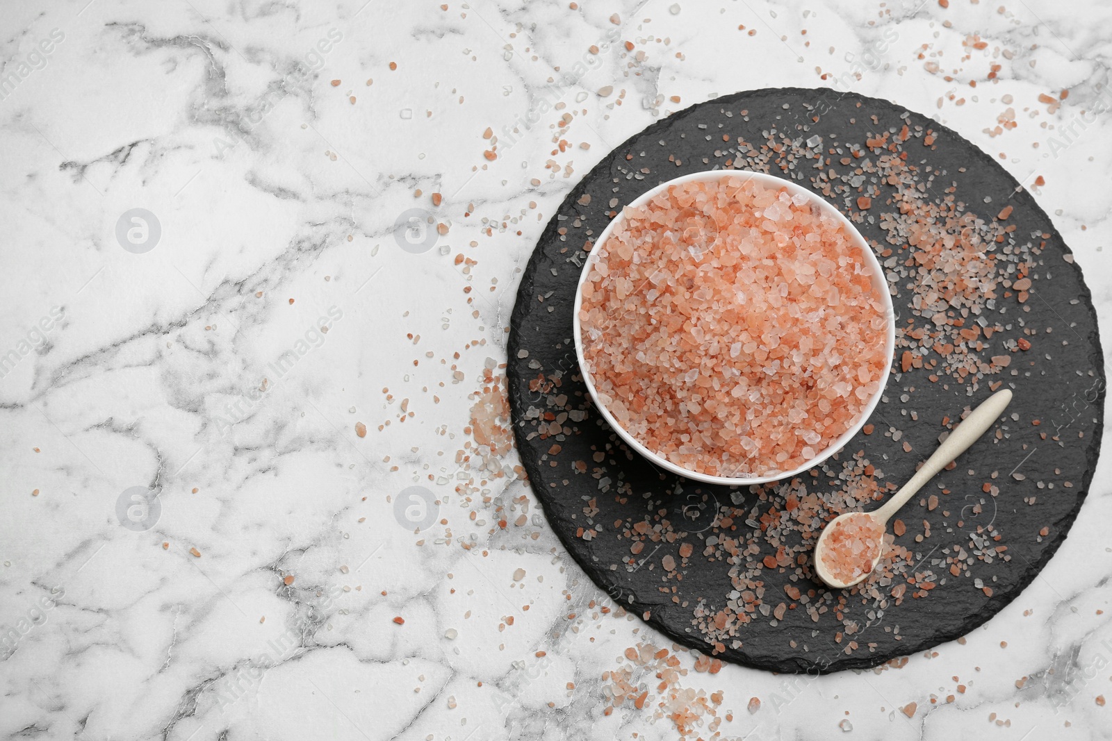 Photo of Spoon and bowl with pink himalayan salt on white marble table, flat lay. Space for text