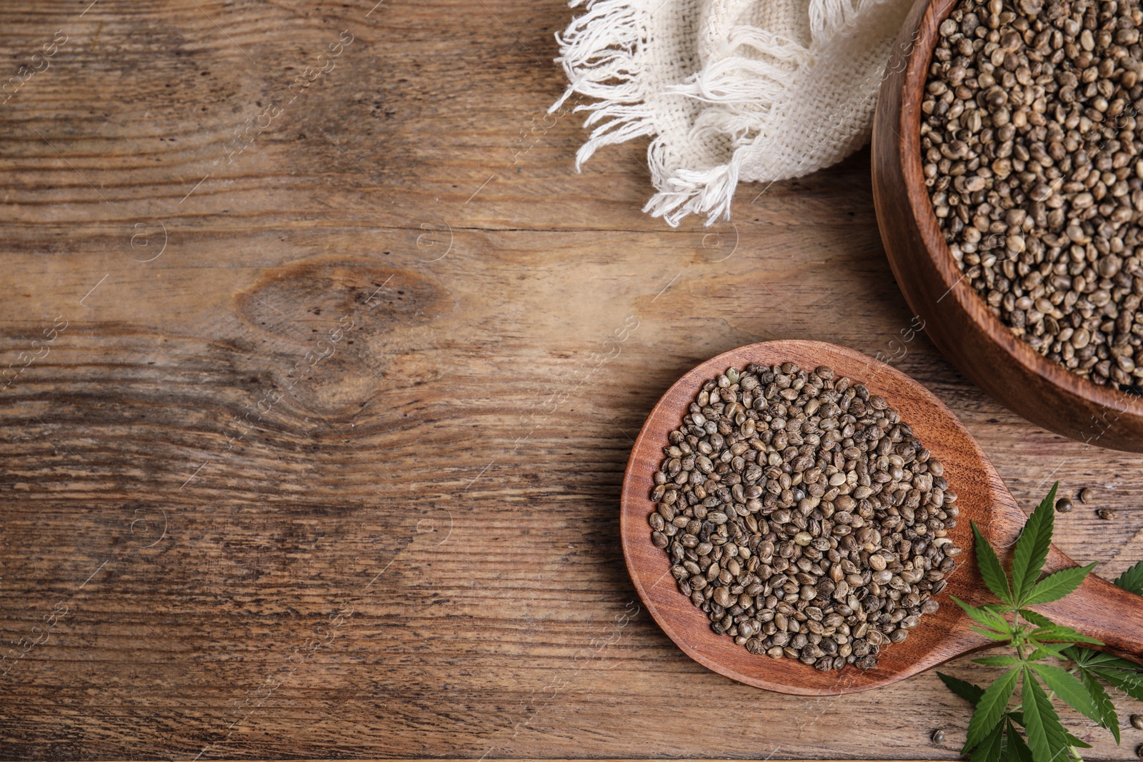 Photo of Organic hemp seeds and leaves on wooden table, flat lay. Space for text