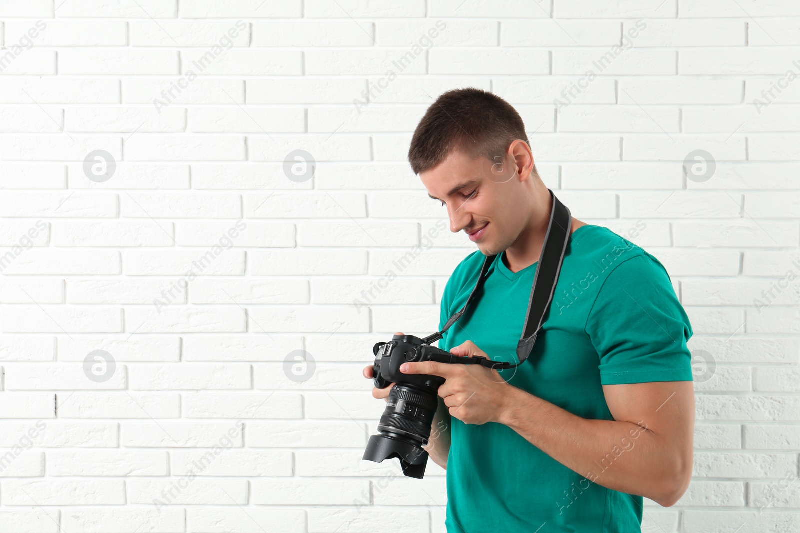 Photo of Young photographer with professional camera near brick wall. Space for text