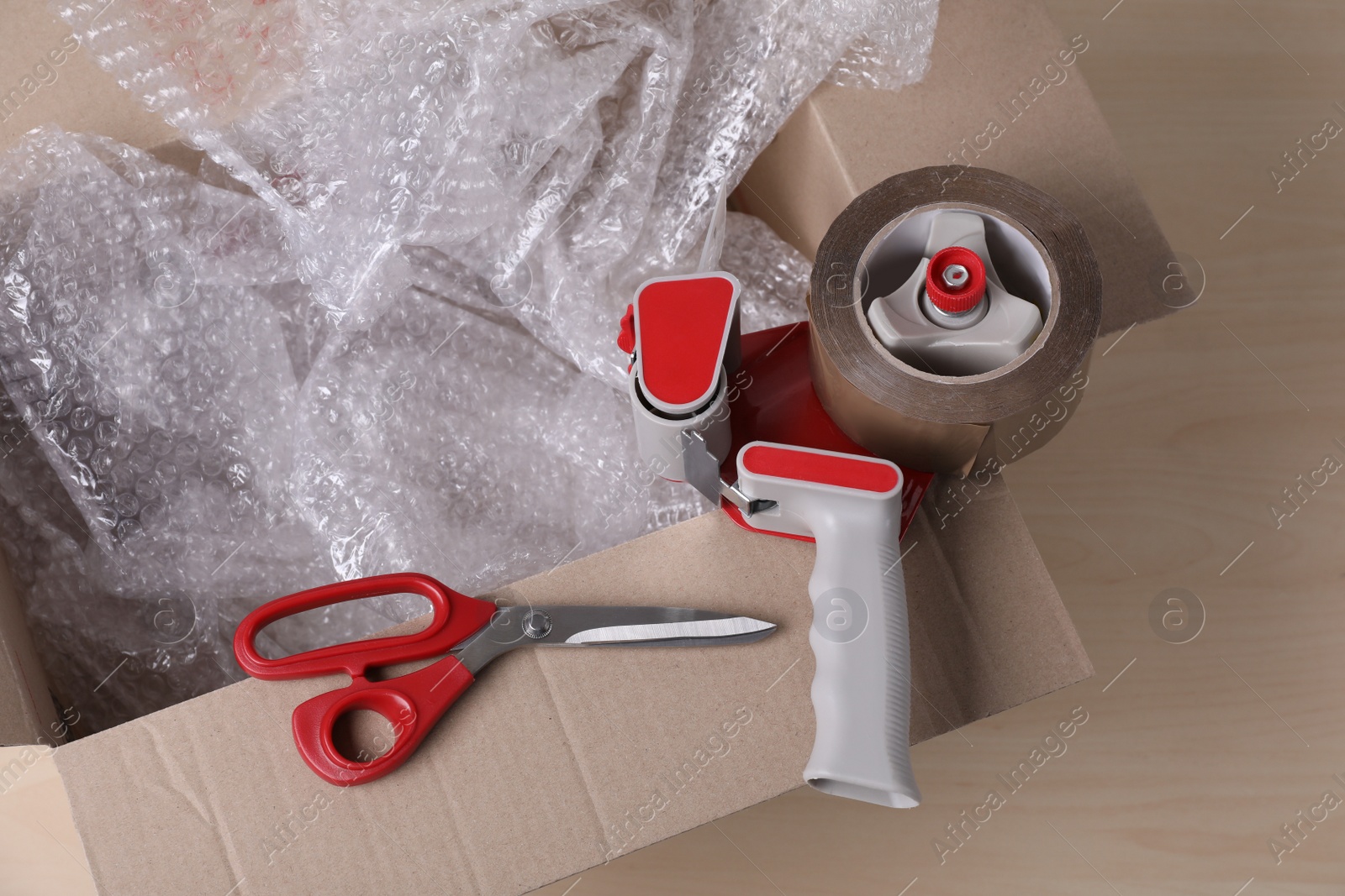 Photo of Cardboard box with bubble wrap, scissors and adhesive tape on wooden table