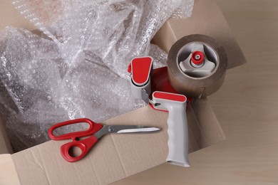 Cardboard box with bubble wrap, scissors and adhesive tape on wooden table