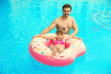 Father and daughter with inflatable ring in swimming pool