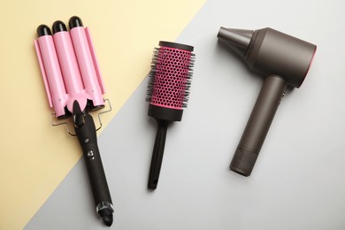 Hair dryer, round brush and triple curling iron on color background, flat lay