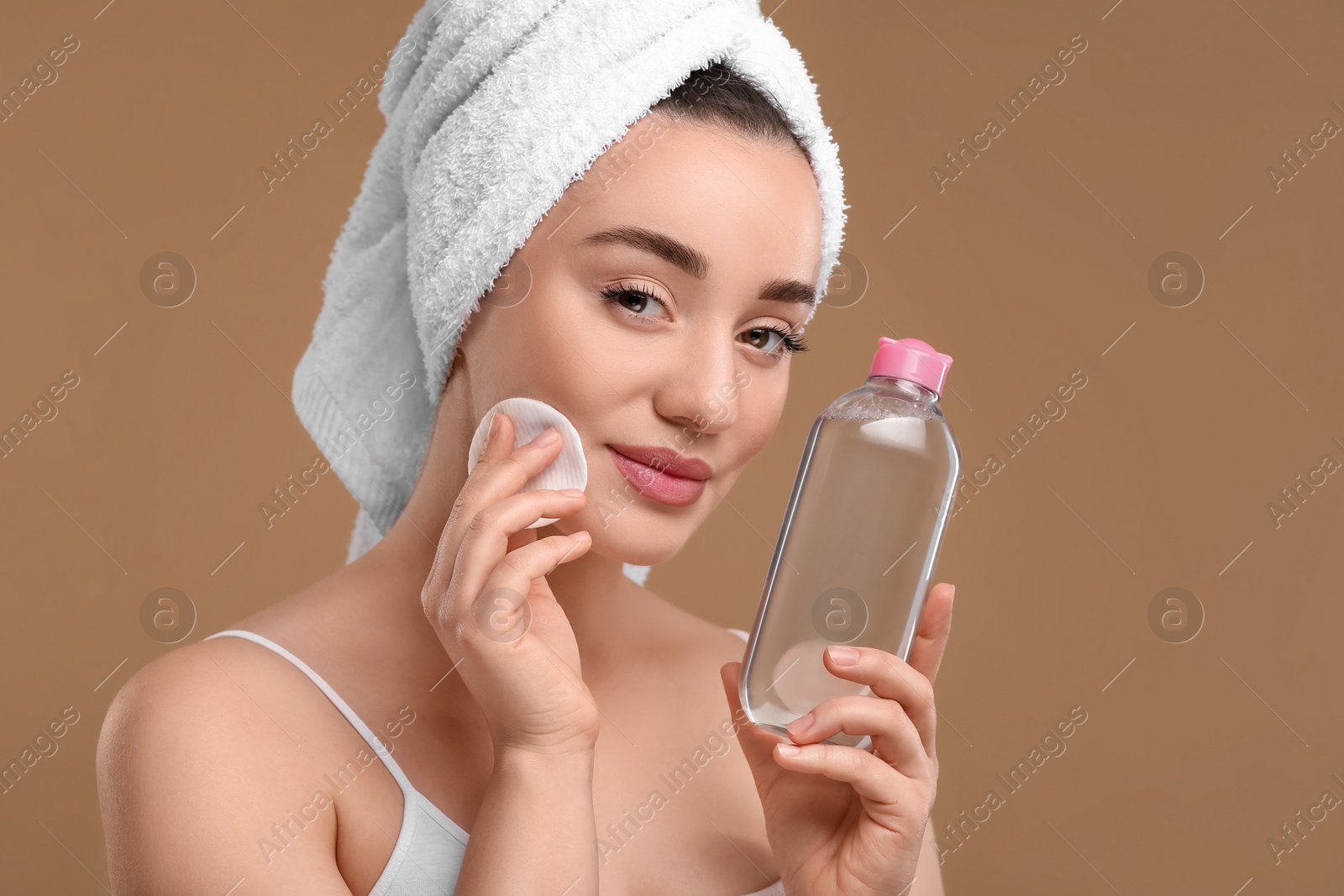 Photo of Beautiful woman in terry towel removing makeup with cotton pad on beige background