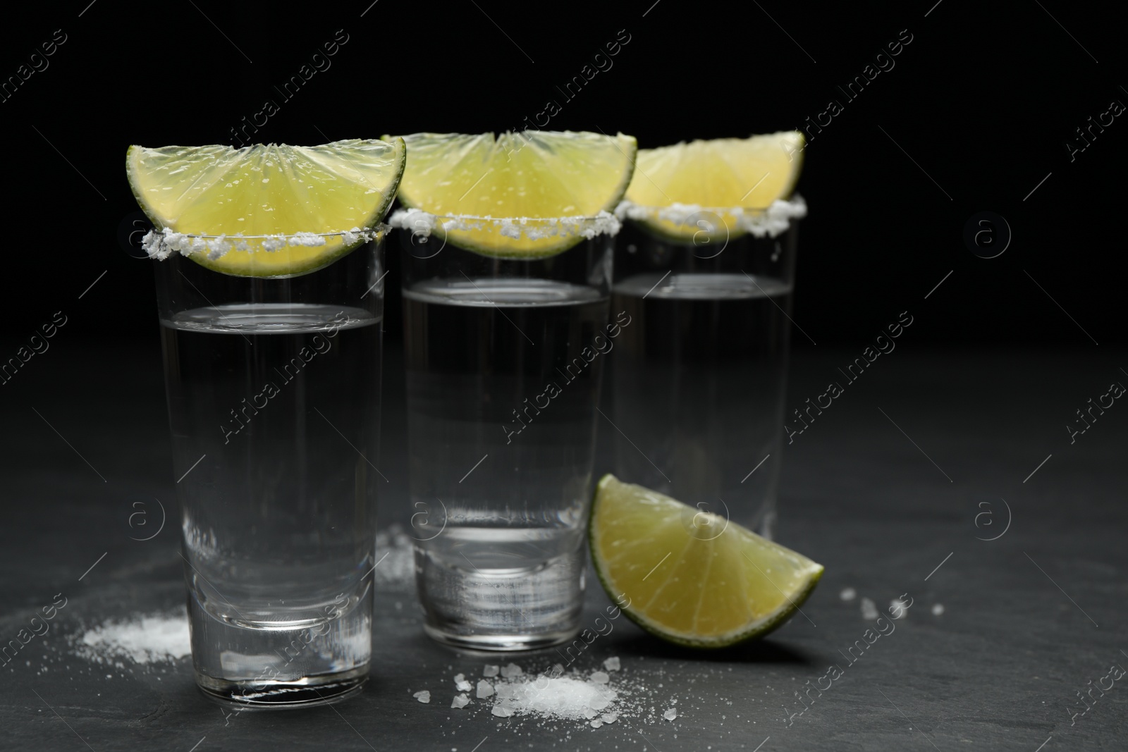 Photo of Mexican Tequila shots, lime slices and salt on black table